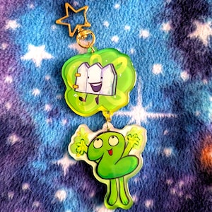 Puede incluir: Un llavero de doble cara con dos personajes de dibujos animados. El dije superior es un diseño verde en forma de nube con un personaje de valla. El dije inferior es un personaje verde con el número dos. El llavero tiene un cierre dorado en forma de estrella.