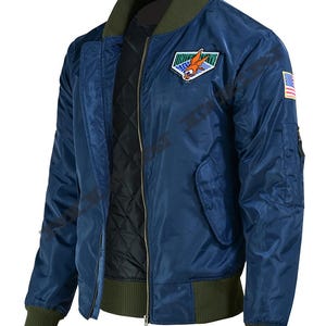 May include: A navy blue bomber jacket with a green collar, cuffs, and waistband. The jacket features a patch with an eagle and a US flag patch on the sleeve. It has a zipper closure and a quilted black lining.
