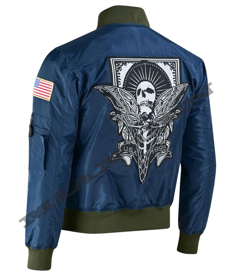 May include: Navy blue bomber jacket with a green collar, cuffs, and hem. Features a large patch on the back with a skull and moth design, and the text "USA 1995". Includes a small American flag patch on the left sleeve.