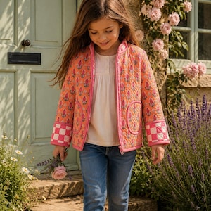 Könnte beinhalten: Eine gesteppte Jacke in Orange mit rosa Blumenmuster, ausgestattet mit einem Frontreißverschluss, zwei abgerundeten Taschen und Ärmelbündchen mit rosa-weißem Karomuster. Die Jacke wird über einem cremefarbenen Hemd und blauen Jeans getragen.
