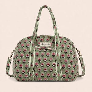 Könnte beinhalten: Eine gesteppte Reisetasche in Salbeigrün mit einem sich wiederholenden Blumenmuster in Rosa und Dunkelrot. Die Tasche hat zwei Tragegriffe und einen abnehmbaren Schultergurt mit grün-weiß gestreifter Kante. Ein weißes Etikett zeigt kit & hop.
