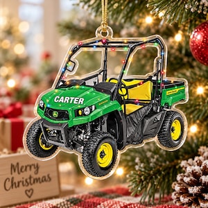 Könnte beinhalten: Ein durchsichtiger Acryl-Weihnachtsbaumschmuck in Form eines grünen und gelben John Deere Nutzfahrzeugs. Das Fahrzeug trägt den Namen CARTER auf der Motorhaube, schwarze Reifen, gelbe Sitze und eine Lichterkette, die über den Rahmen drapiert ist.