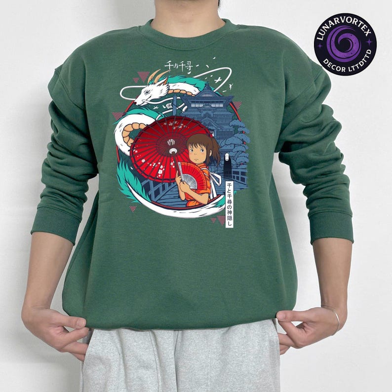 K&ouml;nnte beinhalten: Gr&uuml;nes Sweatshirt mit einem farbenfrohen Grafikdesign aus dem Anime-Film Spirited Away. Das Design zeigt einen roten Regenschirm, einen Drachen und japanischen Text. Das Sweatshirt hat lange &Auml;rmel und einen Rundhalsausschnitt.