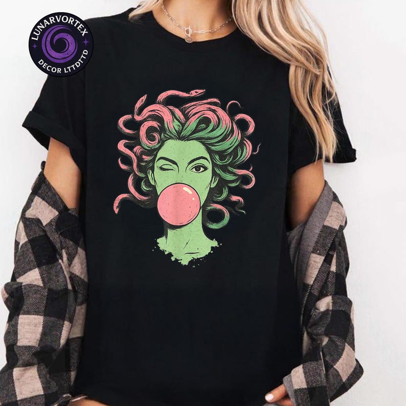 May include: Black t-shirt featuring a graphic of a winking woman with green skin, pink and green hair, and a pink bubblegum bubble. The design is a stylized illustration of Medusa. The shirt has a crew neck and short sleeves.