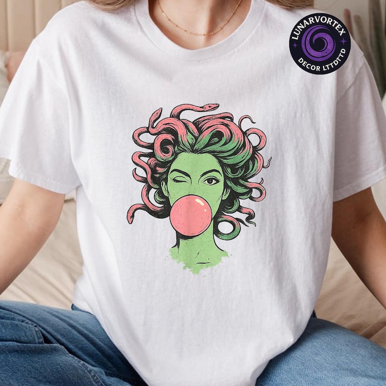 May include: White t-shirt featuring a graphic of a green-skinned woman with pink and green snake hair blowing a pink bubble. The woman is winking. The shirt has a round neck and short sleeves. The brand logo is in the upper right corner.