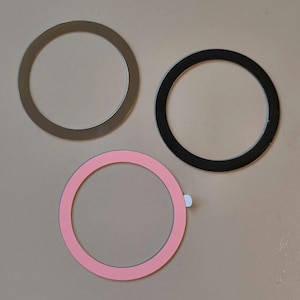 May include: Three circular rings are shown. One is silver, one is black, and the third is pink. The pink ring has a small white tab attached. The rings are of similar size and are arranged in a triangular pattern.