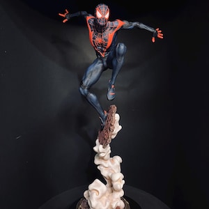 Puede incluir: Una detallada figura de Spider-Man en una pose din&aacute;mica, saltando desde una base en forma de nube. La figura es predominantemente azul marino con acentos rojos, incluyendo el emblema de la ara&ntilde;a en el pecho. La base es una mezcla de marr&oacute;n y crema.