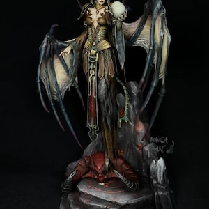 May include: A detailed figurine of a demonic female figure with large wings, horns, and a skull. The figure is standing on a rock formation with a red demon at its base. The color palette includes shades of brown, gold, and black.