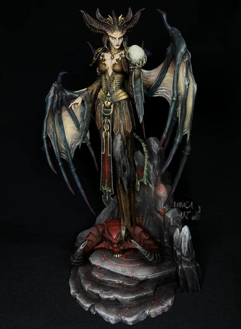 May include: A detailed figurine of a demonic female figure with large wings, horns, and a skull. The figure is standing on a rock formation with a red demon at its base. The color palette includes shades of brown, gold, and black.