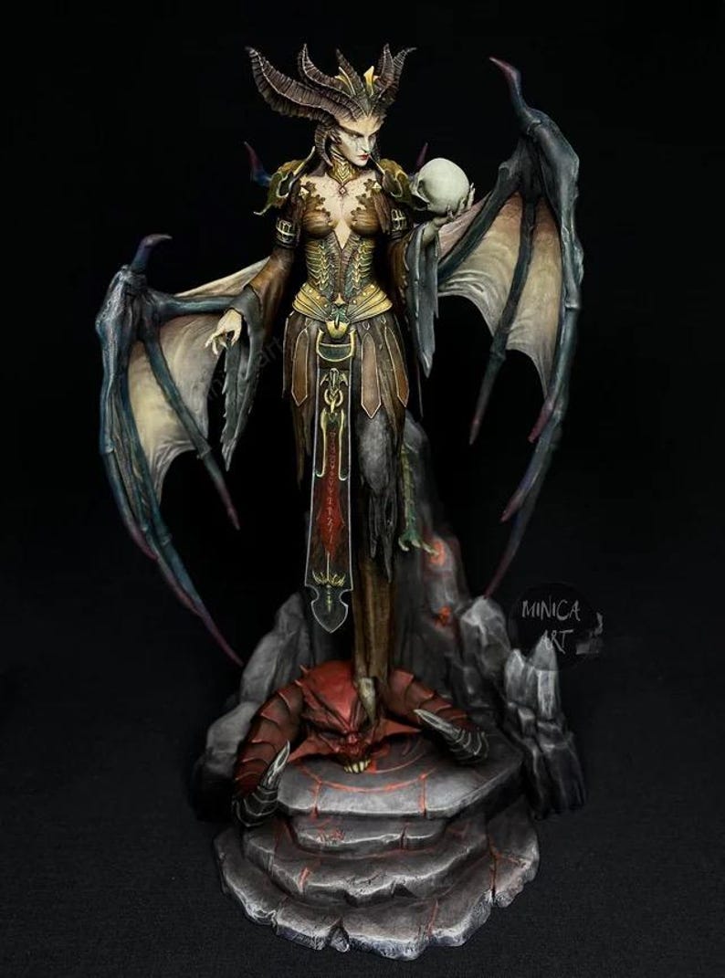 May include: A detailed figurine of a demonic female figure with large wings, horns, and a skull. The figure is dressed in a brown and gold outfit and stands on a stone base with a red demon. The artwork is signed "MINICA ART".