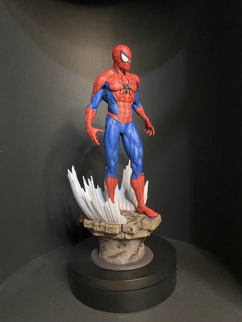 Pode incluir: Uma figura detalhada do Homem-Aranha numa pose cl&aacute;ssica. A figura &eacute; predominantemente vermelha e azul, com um emblema de aranha preta no peito. Est&aacute; sobre uma base rochosa com elementos brancos estilizados em forma de teia.