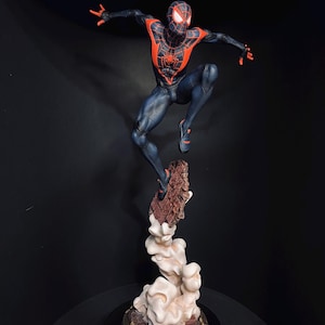 Puede incluir: Una figura din&aacute;mica de un superh&eacute;roe con un traje negro y rojo, en plena acci&oacute;n. La figura est&aacute; sostenida por una base detallada con un efecto de nube, creando una sensaci&oacute;n de movimiento. La pose y el dise&ntilde;o del superh&eacute;roe sugieren un tema de c&oacute;mic o pel&iacute;cula.