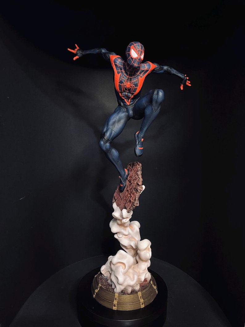 Puede incluir: Una figura din&aacute;mica de un superh&eacute;roe con un traje negro y rojo, en plena acci&oacute;n. La figura est&aacute; sostenida por una base detallada con un efecto de nube, creando una sensaci&oacute;n de movimiento. La pose y el dise&ntilde;o del superh&eacute;roe sugieren un tema de c&oacute;mic o pel&iacute;cula.