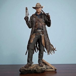 May include: A detailed figurine of a character in a cowboy hat and long coat, holding two guns. The figure is dressed in a dark outfit with brown accents, standing on a rocky base. The background is a solid light blue.