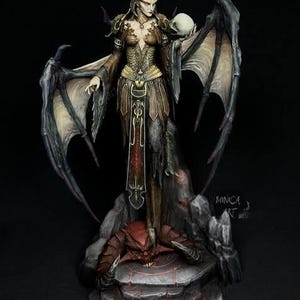 May include: A detailed fantasy figurine of a horned demon woman with large wings, holding a skull. The figure is dressed in ornate armor and stands atop a stone base with a red demon. The artwork is dark and detailed.