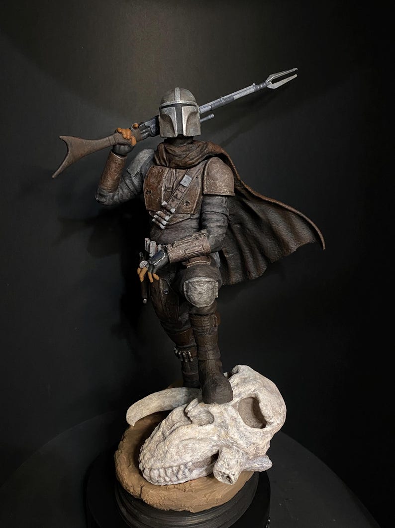 May include: A detailed figurine of a character in a helmet and armor, holding a rifle over their shoulder. The figure stands on a skull-shaped base. The color palette includes shades of gray, brown, and black, with a dark background.