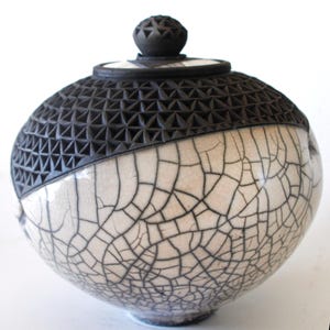 Tarro cubierto con la técnica raku blanca craquelada y con motivos negros grabados que contrastan entre sí.