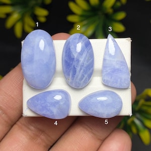 May include: Five polished, light blue gemstones of varying shapes are displayed on a white surface. The gemstones include oval, teardrop, and triangular shapes. The stones have a translucent quality with subtle internal patterns.