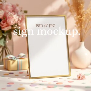 May include: A gold-framed sign mockup with the text "sign mockup" and "PSD & JPG" on a white background. The scene includes a vase of pink flowers, a gift box, and confetti, creating a soft, inviting aesthetic.