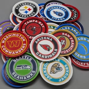 Op de afbeelding: Een verzameling ronde onderzetters met diverse NFL-teamlogo's en namen, waaronder de Pittsburgh Steelers, Tampa Bay Buccaneers, Washington Commanders, Arizona Cardinals, Seattle Seahawks en Jacksonville Jaguars.