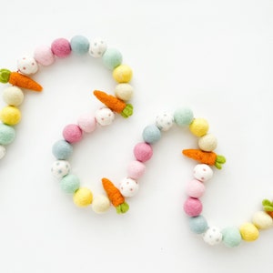 May include: A garland of pastel coloured felt balls with carrot accents. The garland is made of felt and is perfect for decorating for Easter.