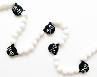 May include: A black and white garland with black felt cat faces and white pom poms.