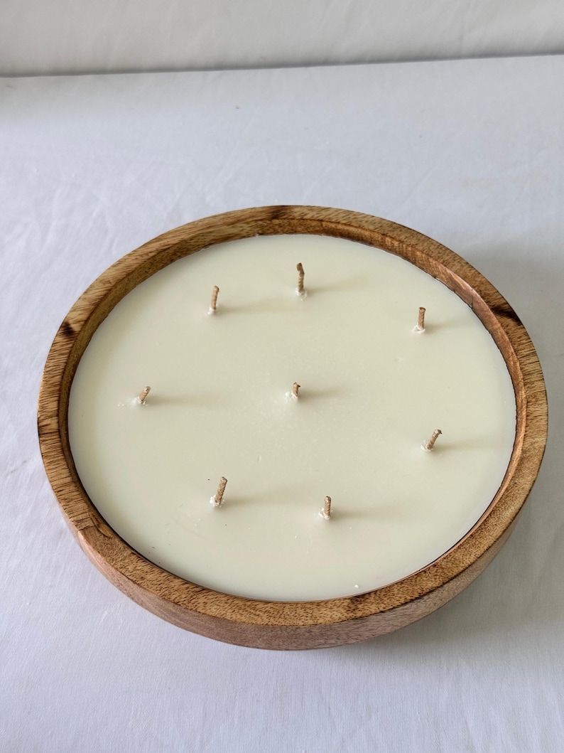 May include: A large, round candle with eight wicks, set in a natural wood bowl. The candle wax is a creamy off-white color. The wooden bowl has a warm, light brown tone, creating a rustic aesthetic. The candle is designed for home fragrance.