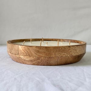 May include: A large, round wooden candle with multiple wicks. The candle is housed in a natural wood bowl, showcasing the wood grain. The candle's wax is a creamy white color, and the wicks are visible.