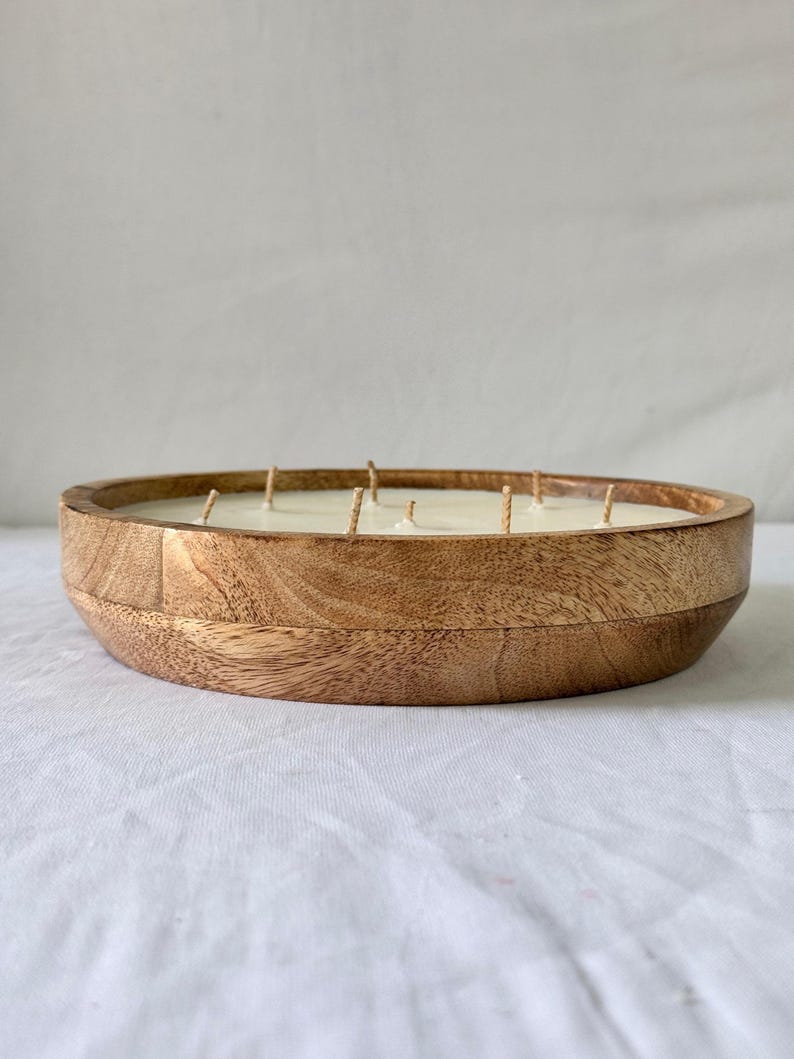 May include: A large, round wooden candle with multiple wicks. The candle is housed in a natural wood bowl, showcasing the wood grain. The candle's wax is a creamy white color, and the wicks are visible.