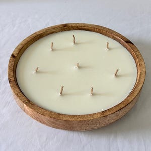 May include: A large, round candle with seven wicks, set in a natural wood bowl. The candle wax is a creamy off-white color, and the wooden bowl has a warm, brown tone. This decorative candle is ideal for home decor and creating a relaxing ambiance.