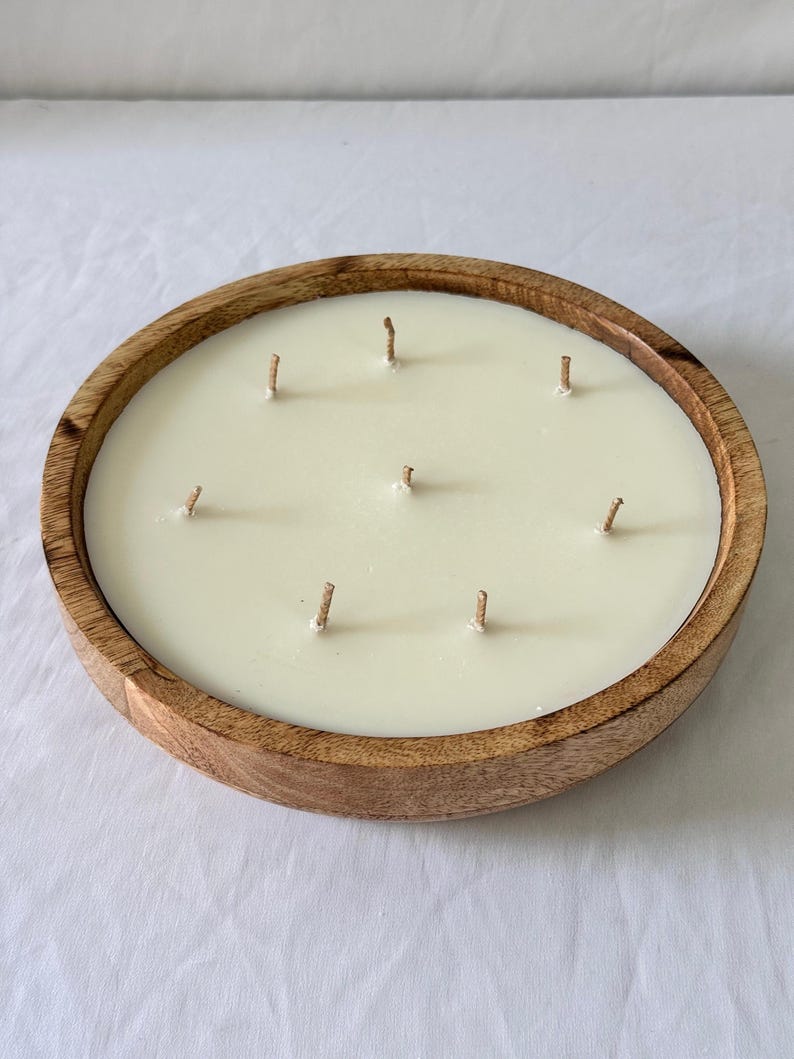 May include: A large, round candle with seven wicks, set in a natural wood bowl. The candle wax is a creamy off-white color, and the wooden bowl has a warm, brown tone. This decorative candle is ideal for home decor and creating a relaxing ambiance.