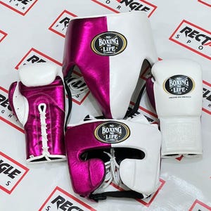 Op de afbeelding: Set boksuitrusting met een witte en magenta hoofdbeschermer, kruisbeschermer en bokshandschoenen. De handschoenen en hoofdbeschermer hebben de tekst "NO BOXING NO LIFE". De handschoenen zijn wit met magenta accenten.