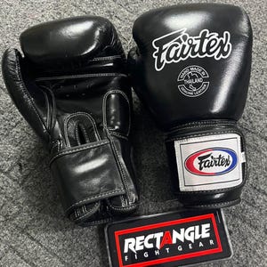 May include: Pair of black Fairtex boxing gloves with white stitching. The gloves have the Fairtex logo in white and a label that says "Hand Made in Thailand Genuine Leather". A Rectangle Fight Gear logo is visible.