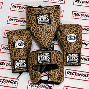 May include: A set of Cleto Reyes professional boxing equipment featuring a leopard print pattern. The set includes two boxing gloves, a groin protector, and a headgear piece, each displaying the black and white Cleto Reyes brand logo.