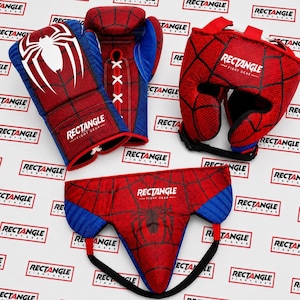 Op de afbeelding: Een set rode en blauwe boksuitrusting met een spinnenwebpatroon en de witte tekst RECTANGLE FIGHT GEAR. De set bevat twee bokshandschoenen met witte vetersluiting, een hoofdbeschermer en een tok met zwarte banden.