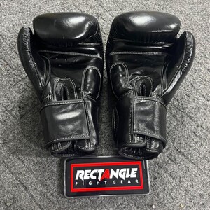 May include: A pair of black boxing gloves with white stitching. The gloves are made of a shiny material and have a hook-and-loop closure. A rectangular sign with the text "RECTANGLE FIGHT GEAR" is at the bottom.