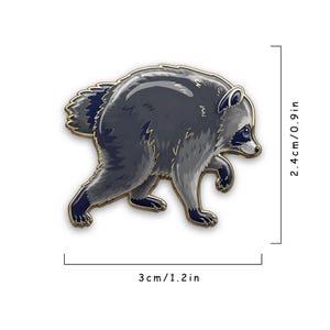 May include: A raccoon-shaped enamel pin with dark gray and light gray fur, black eye markings, and gold-toned metal edges. The pin measures 1.2 inches in width and 0.9 inches in height, as indicated by the printed dimension text and lines.