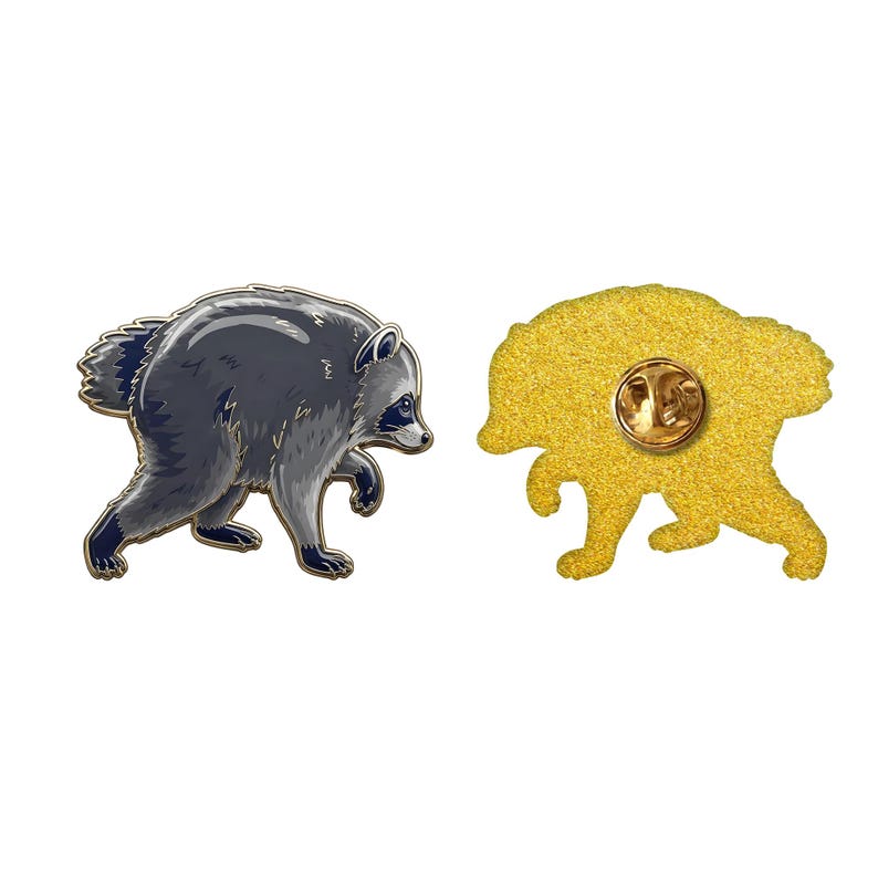 May include: A metal enamel pin shaped like a raccoon in a walking pose, featuring gray and black fur details. The reverse side is textured gold-tone metal with a single pin post and a circular clutch back for secure attachment to fabric.
