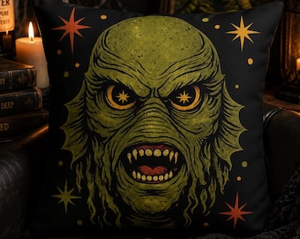 May include: A square throw pillow with a black background featuring a large, detailed illustration of a green, scaly creature with sharp teeth and glowing yellow eyes. The design includes small orange and yellow star shapes scattered around.