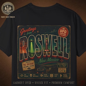 May include: Black t-shirt featuring a vintage-style Roswell, New Mexico design. The graphic includes a UFO, the text "Greetings from Roswell," and other details related to the town's alien lore. The shirt is garment dyed, unisex fit, and premium comfort.