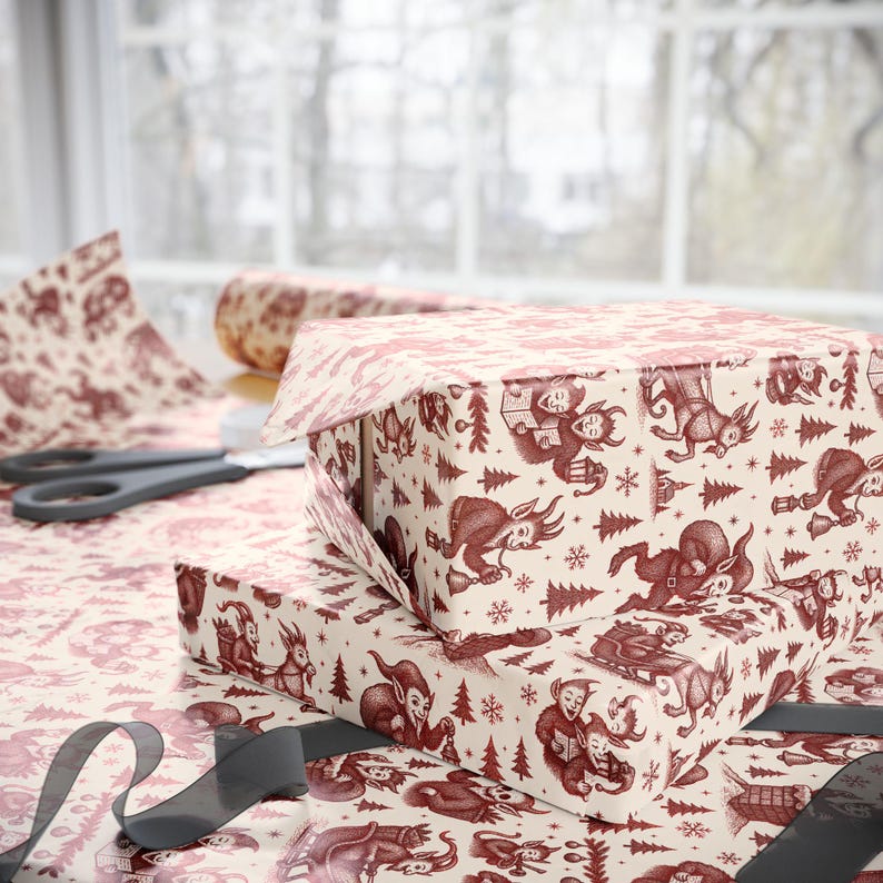 May include: Two gift boxes wrapped in cream-colored paper with a repeating pattern of red illustrations of elves, trees, and snowflakes. A roll of matching wrapping paper and scissors are visible in the background. A gray ribbon is in the foreground.