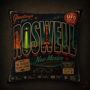 May include: A decorative pillow with a vintage design featuring the word "Roswell" in large letters. The pillow has a dark background with illustrations of a UFO, motel, and desert landscape. Text includes "Greetings from Roswell, New Mexico."