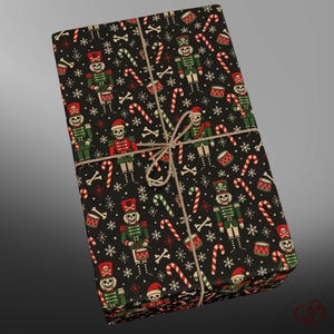 May include: A rectangular gift box wrapped in black paper featuring a repeating pattern of skeleton nutcrackers, candy canes, drums, and white snowflakes. The package is tied with a simple brown twine string centered across the top surface.