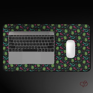 May include: A black rectangular mousepad with a repeating pattern of green vampire faces, pink high heels, and blue bats. A silver laptop and white mouse are on the mousepad.