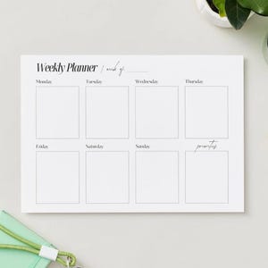 Könnte beinhalten: Ein weißer Wochenplaner mit dem Text "Weekly Planner / week of" oben. Der Planer hat Kästchen für jeden Wochentag, mit "priorities" unten. Ein Bleistift, ein grüner Notizblock und ein Glas sind ebenfalls sichtbar.