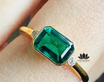 May include: A gold ring featuring a rectangular, emerald-cut green gemstone as the primary focal point. Two smaller, round, clear gemstones flank the main stone. The ring has a slender gold band.