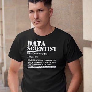 May include: Black t-shirt with the text "DATA SCIENTIST" in white. The shirt includes a definition of a data scientist, and the words "SEE ALSO: NINJA; BADASS; LEGEND". The person is wearing a gold chain.