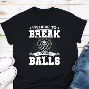 May include: Black t-shirt with white text that reads "I'M HERE TO BREAK YOUR BALLS". The design includes a graphic of billiard balls and crossed pool cues. The shirt is paired with white trainers and blue jeans.