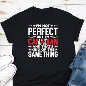 May include: Black t-shirt with the text "I'M NOT PERFECT BUT I'M CANADIAN AND THAT'S KIND OF THE SAME THING" in white and red. The shirt is paired with white sneakers and blue jeans.