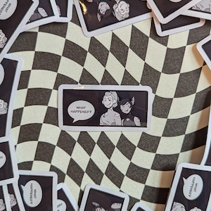 Op de afbeelding: Een verzameling rechthoekige stickers en kaarten met stripfiguren. De centrale sticker toont twee personages met de tekst "WHAT HAPPENED?". De achtergrond is een zwart-wit geblokt patroon.